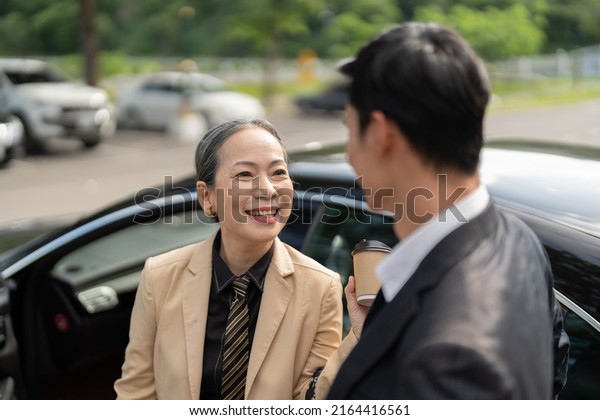 Happy senior\
old asian businesswoman discussion talking about new project with\
young asian male colleague at car\
park.