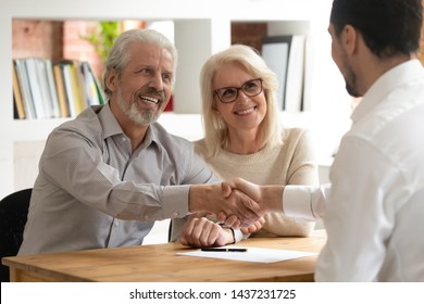Happy senior old family couple clients make financial insurance estate business deal handshake agent lawyer, satisfied mature customers shake hand meeting bank manager agree on investment contract