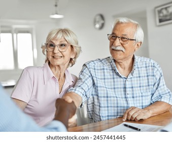 Happy senior old family couple clients make financial insurance estate business deal contract signing and shaking hands, agent lawyer, satisfied mature customers signing contract meeting bank manager  - Powered by Shutterstock