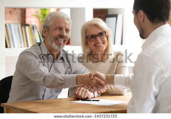 Happy senior old family couple clients make\
financial insurance estate business deal handshake agent lawyer,\
satisfied mature customers shake hand meeting bank manager agree on\
investment contract