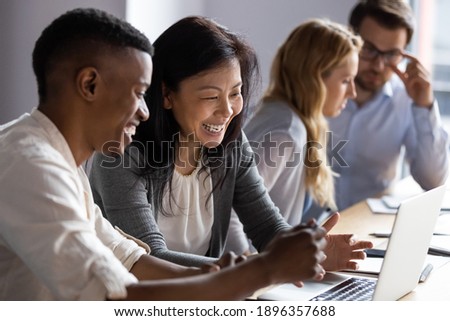 Happy senior old korean businesswoman discussing online project on laptop with african american male colleague, working together in pairs at shared workplace, analyzing electronic documents.