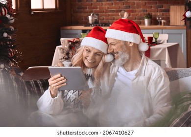 Happy senior old mature 50s grandparents couple holding using digital tablet laughing feeling joy having virtual party celebrate Christmas on video family call sitting on couch at home in living room. - Powered by Shutterstock