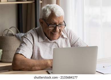 Happy senior older 80s man in glasses using laptop computer at work desk, typing, smiling, laughing, making video call, enjoying online talk, virtual chat, watching webinar, training on internet - Powered by Shutterstock