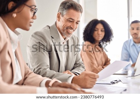 Happy senior older Indian businessman investor bank client checking document at office team meeting with financial law experts attorneys team. Consultancy and advisory services concept.