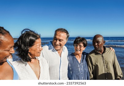 Happy senior people having fun walking on the beach at sunset wearing summer clothes - Joyful elderly lifestyle, vacation and travel concept - Main focus on center friends faces - Powered by Shutterstock