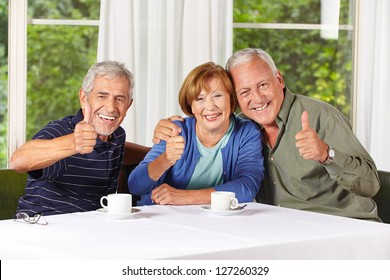 Happy senior people holding thumbs up while drinking coffee in retirement home
