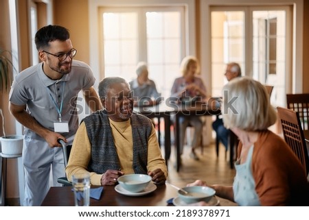 Happy senior people and their caregiver talking in dining room at nursing home.