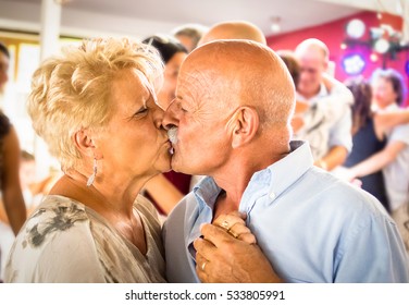 Happy senior retired couple having fun on dancing at restaurant wedding celebration party - Love concept of joyful elderly and retirement lifestyle with man lovely kissing wife - High iso color image - Powered by Shutterstock