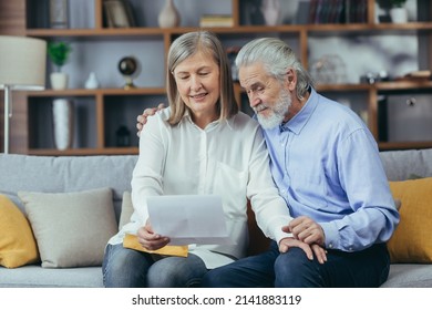 Happy Senior Retired Couple Sitting On Sofa At Home Reading Letter, Happy And Smiling