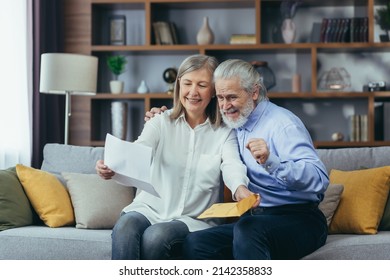 Happy Senior Retired Couple Sitting On Sofa At Home Reading Letter, Happy And Smiling