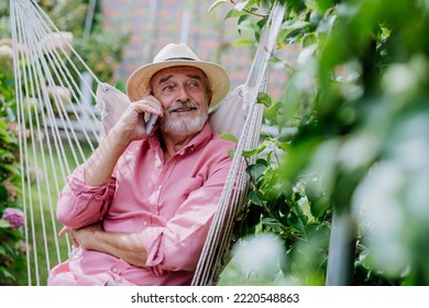 Happy Senior Sitting In Outdoor Garden Swing And Phoneing.