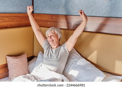 Happy senior smiling woman with short gray hair stretching oneself after sleeping in bed, enjoying sunshine. At home, in hotel, in camping. Elderly, concept - Shutterstock ID 2244666981