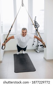 Happy Senior Sportsman Takes Exercise With Trx. Full Length. Strong Man Does Crossfit Push Ups With Fitness Straps For Suspension Training. Workout At Home. Active And Healthy Lifestyle.