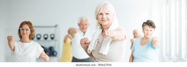 Happy Senior Sportswoman With A Towel Around Her Neck Exercising With Friends In A Fitness Studio