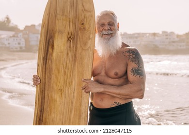 Happy Senior Surfer Man Holding Vintage Wood Surf Board On The Beach - Focus On Face