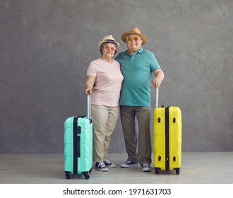 Happy senior tourists ready for vacation and adventure trip. Old retired married couple in sun hats and glasses with mint green and yellow travel suitcases standing in studio with gray background - Powered by Shutterstock