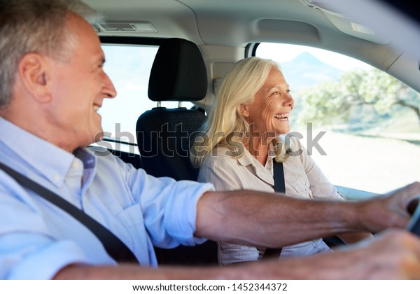 Happy senior white couple driving in their car,\
smiling, side view, close\
up