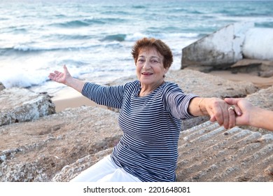 Happy Senior Woman 80+ At The Seaside With Arms Wide Open, Holding On To Friend. Concept Of Support, Health Insurance, Quality Of Life, Travel In Old Age. Caucasian. Emotional, Smiley Face. Soft Focus