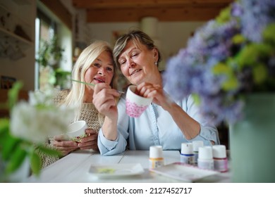 Happy senior woman artist teaching her friend how to paint cermaic cup, artcraft concept. - Powered by Shutterstock