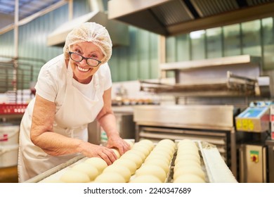 Happy senior woman as a baker with experience baking rolls in the large bakery - Powered by Shutterstock