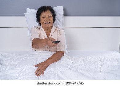 happy senior woman in bed with remote control and watching tv