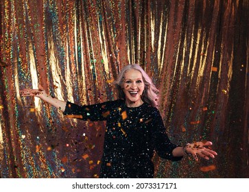 Happy Senior Woman In Black Dress Standing Under Confetti Against A Golden Backdrop