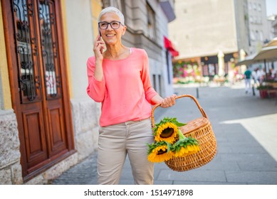 Happy Senior Woman Calling On Smartphone In Summer City Street - Retirement, Communication And Old People Concept. Senior Woman Using Her Mobile Phone On A Sunny Day