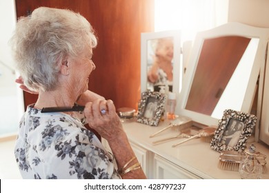 Happy Senior Woman Combing Her Hair At Dresser In House. Elderly Female Getting Ready In Front Of A Mirror At Home.