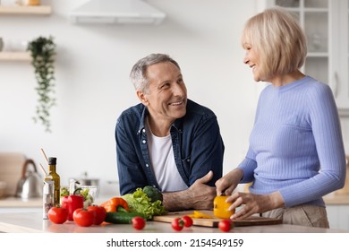 Happy Senior Woman Cooking For Her Husband, Cutting Vegetables, Handsome Mature Man Waiting For Delicious Healthy Dinner, White Cozy Kitchen Interior, Copy Space. Family Lifestyle Concept