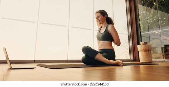 Happy senior woman doing a cow face pose during an online yoga class at home. Smiling mature woman practicing a stretching asana on a yoga mat. Woman following a virtual workout tutorial on a laptop. - Powered by Shutterstock