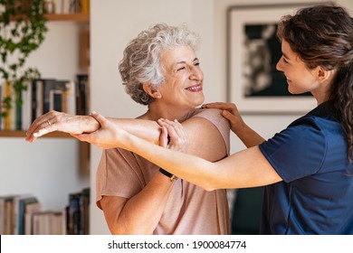 Happy senior woman doing exercise at home with physiotherapist. Old retired lady doing stretching arms at home with the help of a personal trainer during a rehabilitation session.