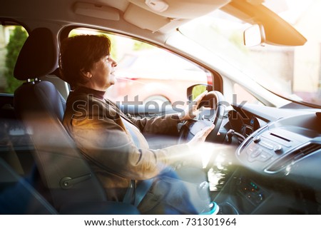 Happy senior woman driving a car through the city.