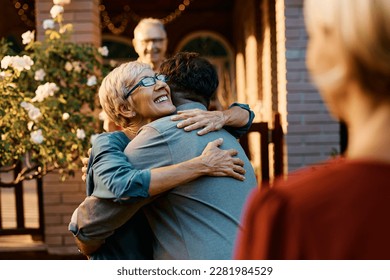 Happy senior woman embracing her son while welcoming him and his wife in front of the house. - Shutterstock ID 2281984529