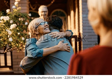 Happy senior woman embracing her son while welcoming him and his wife in front of the house.