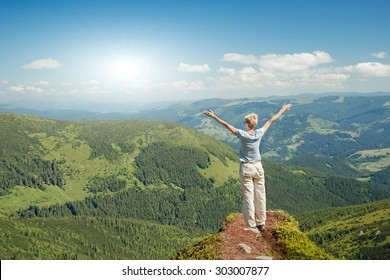 Happy Senior Woman Enjoying The Nature In The Mountains And Looking On Sky With Raised Hands. Freedom Concept