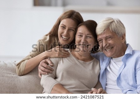 Happy senior woman enjoying warm good relationship with adult daughter and loving older husband, posing with family for shooting, looking away, smiling, laughing