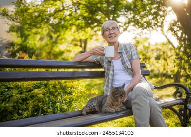 Happy senior woman enjoys drinking coffee and spending time with her cat while sitting on a bench in her garden. - Powered by Shutterstock