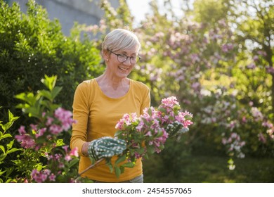 Happy senior woman enjoys looking at flowers in her garden. - Powered by Shutterstock