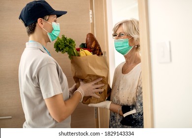 Happy senior woman and female courier wearing face masks during groceries home delivery due to coronavirus pandemic.  - Powered by Shutterstock