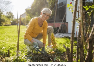 Happy senior woman gardening in her yard. She is using rake. - Powered by Shutterstock