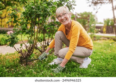 Happy senior woman gardening in her yard. She is using rake.	 - Powered by Shutterstock