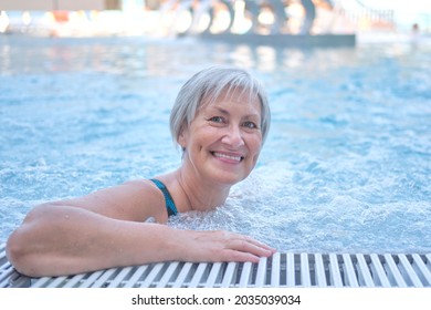 Happy senior woman with gray hair looking at camera in outdoor thermal pool with hydromassage. Active ageing concept.