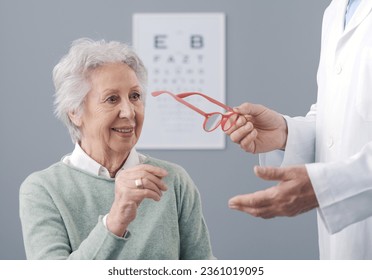 Happy senior woman having an eye exam, the doctor is giving her a new pair of prescription glasses - Powered by Shutterstock