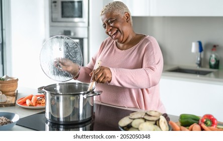 Happy senior woman having fun preparing lunch in modern kitchen - Hispanic Mother cooking for the family at home