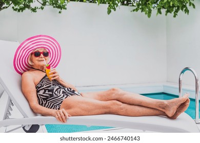 Happy senior woman having party in the swimming pool - Beautiful senior lady sunbathing and relaxing in a private pool during summertime - Powered by Shutterstock