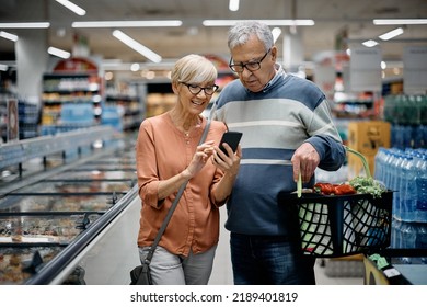 Happy senior woman and her husband using app on mobile phone while shopping in supermarket.  - Powered by Shutterstock