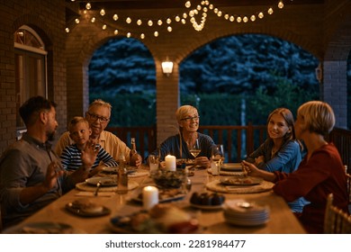 Happy senior woman and her multigeneration family talking while having dinner on a patio. - Powered by Shutterstock