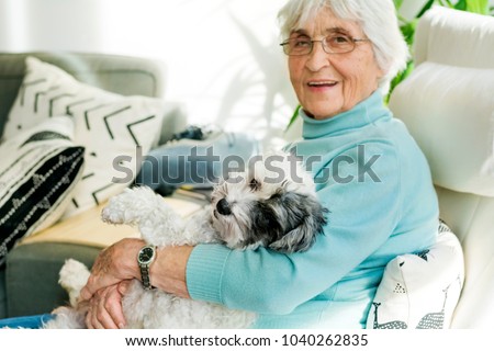 Happy Senior Woman Hugging her Poodle Dog at Home.