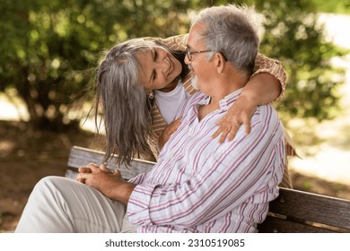 Happy senior woman hugging man in casual, sit on bench, enjoy walk together in park outdoor. Love relationships, retirement, free time and weekend, lifestyle and date, ad, offer - Shutterstock ID 2310519085