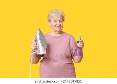 Happy senior woman with iron and spray bottle of water on yellow background - Powered by Shutterstock